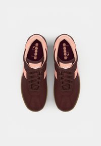 Maroon suede athletic shoes with pink accents and laces. The sole is gum-colored. Features a logo on the tongue and a padded collar.