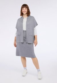 Harmaa vetoketjullinen takki lyhyillä hihoilla ja kahdella etutaskulla, yhdistettynä yhteensopivaan harmaaseen polvimittaseen hameeseen. Mallilla on valkoiset lenkkarit.