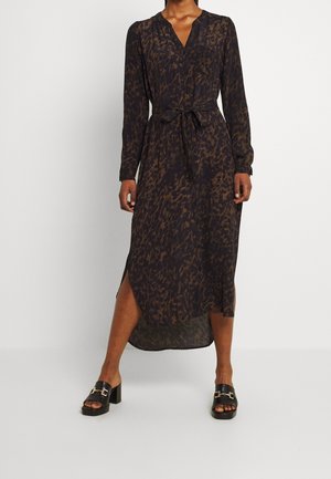 Woman wearing long-sleeve, dark brown and black leopard-print midi dress with side slit and black heeled sandals with gold buckle details.