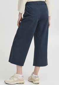 Pantalons en coton bleu marine à jambes larges, avec une coupe décontractée, dotés d'une taille élastique et de poches arrière. Portés avec des baskets de couleur claire.