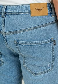 Los jeans de mezclilla azul claro cuentan con un parche de cuero en la cintura, costuras de contraste y un bolsillo trasero con una sola costura que tiene una etiqueta con el logo.