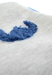 Tissu gris avec une broderie texturée bleue en forme de croissant, présentant une finition douce et duveteuse sur un fond lisse.