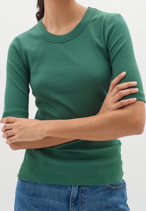 Zielony prążkowany top z okrągłym dekoltem i krótkimi rękawami; dopasowany krój, teksturowana tkanina, zestawiony z niebieskim dżinsem w talii.