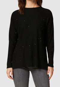 Schwarzer Pullover mit lockerer Passform, der verstreute, glitzernde Akzente, gerippte Bündchen und Saum sowie eine weiche Textur aufweist, kombiniert mit grauen Jeans.