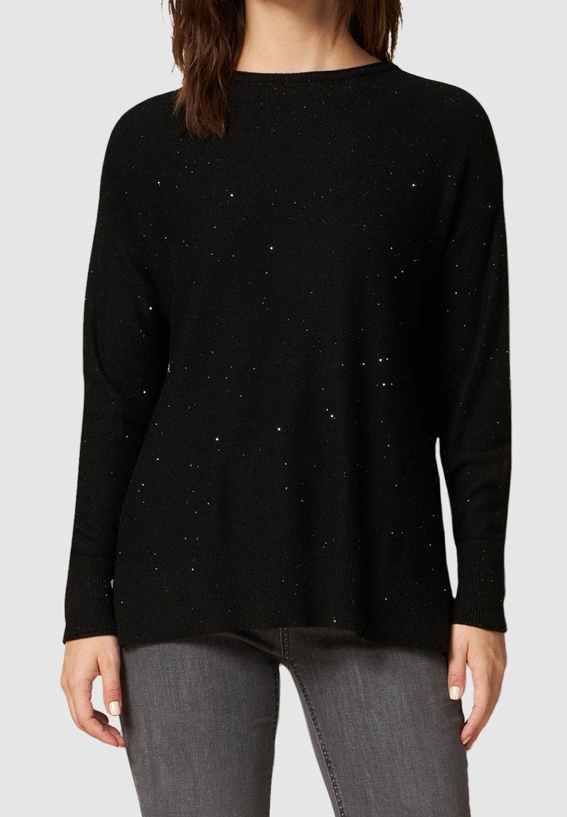 Schwarzer Pullover mit lockerer Passform, der verstreute, glitzernde Akzente, gerippte Bündchen und Saum sowie eine weiche Textur aufweist, kombiniert mit grauen Jeans.