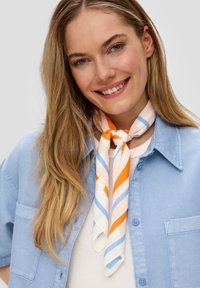 Écharpe en soie avec des rayures diagonales orange, bleu clair et pêche, nouée autour du cou. Portée avec une chemise bleu clair.