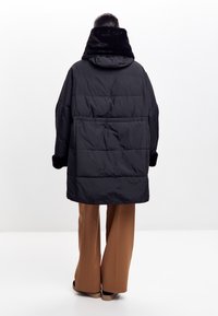 Sort quiltet dunjakke med en blød sort faux fur krave. Har lange ærmer og en løs pasform, parret med lysebrune vide bukser.