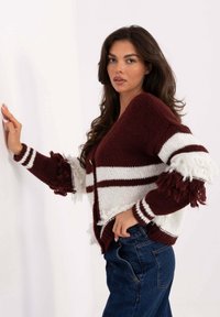 Bordowo-biały, dziergany kardigan z frędzlami na rękawach, zapinany na guziki, o luźnym kroju. Teksturowana tkanina z poziomymi paskami.