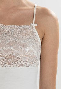 White camisole featuring a lace upper section with floral patterns, thin adjustable straps, and a sleek body-hugging design.