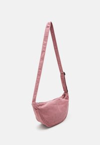 Růžová kordurová kabelka přes rameno s zakřiveným tvarem, nastavitelným popruhem a zapínáním na zip. Má vertikální žebrovanou texturu a prošívané detaily.