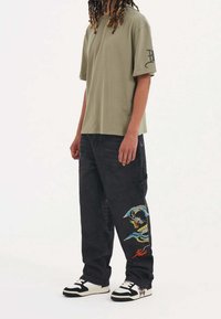 Olivgrön oversized t-shirt, svarta cargobyxor med färgglad drakbroderi, svart och vit sneakers. Enkel, avslappnad passform.