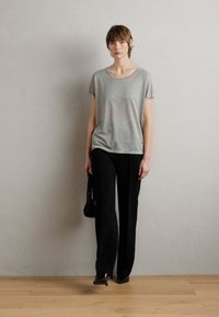 Lichtgrijze T-shirt met korte mouwen, gecombineerd met zwarte broek, met een relaxte pasvorm. Gladde texturen met een minimalistisch ontwerp, geplaatst tegen een neutrale achtergrond.