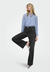 Chemise à rayures bleues et blanches, associée à un pantalon large taille haute noir et des escarpins argentés à bout pointu. Design simple et moderne.