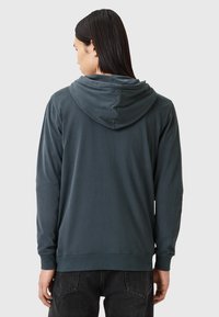 Felpa con cappuccio in tessuto verde scuro, maniche lunghe e polsini a coste. Presenta un taglio casual e una texture morbida e liscia.