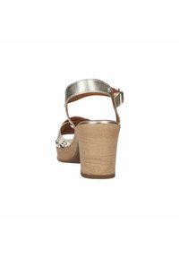 Metalen zilveren wedge sandaal met een verstelbare enkelband, houten hak en decoratieve hardware aan de zijkant. Glad oppervlak en open ontwerp.