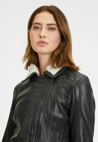 Zwarte leren jas met een nepschapenvachtkraag, ritsluiting en een gestructureerde afwerking met naaddetails. Close-up van het bovenste gedeelte van de jas.