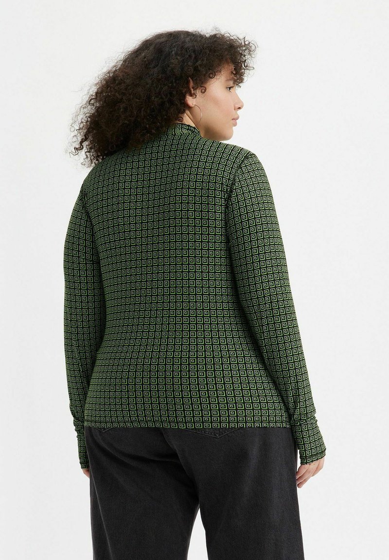 Langärmliges Oberteil aus dunkellangem Material mit geometrischem Muster aus kleinen weißen Quadraten. Mit einem hohen Kragen und figurbetonter Silhouette.