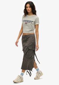 Korte grijze t-shirt met de tekst "SUPERDRY", gecombineerd met een lange, donkergrijze cargorok met zakken en strikaccenten. Draag het met sneakers.