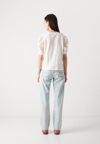 Tricou alb cu mâneci din dantelă, asortat cu blugi albaștri deschis și pantofi roz. Design curat, textură moale și detalii discrete.