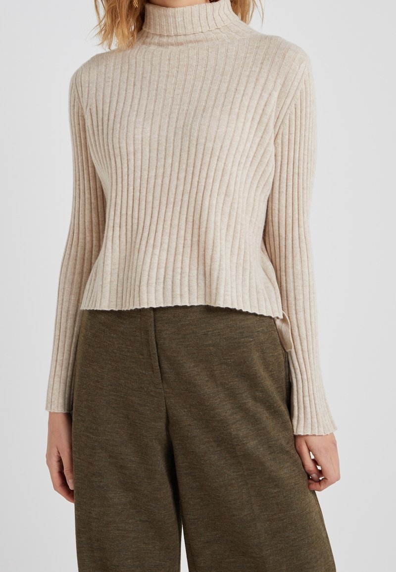 Suéter de cuello alto de canalé beige con mangas largas, corte acortado y textura suave, combinado con pantalones de pierna ancha de color verde olivo.