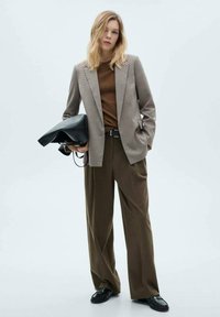 Blazer a scacchi marrone, top in maglia marrone, pantaloni larghi color khaki, scarpe nere e borsa nera. Texture lisce e design su misura.