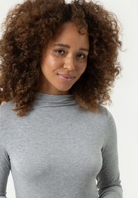 Grijze top met lange mouwen en een hoge hals, gemaakt van een zachte stof. Beschikt over een gladde textuur en een aansluitende pasvorm.