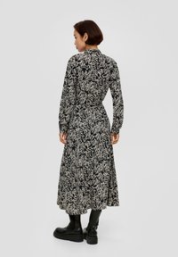 Schwarzes und cremefarbenes Blumenkleid mit langen Ärmeln, Kragen und fließender Silhouette, kombiniert mit glänzenden schwarzen knielangen Stiefeln.