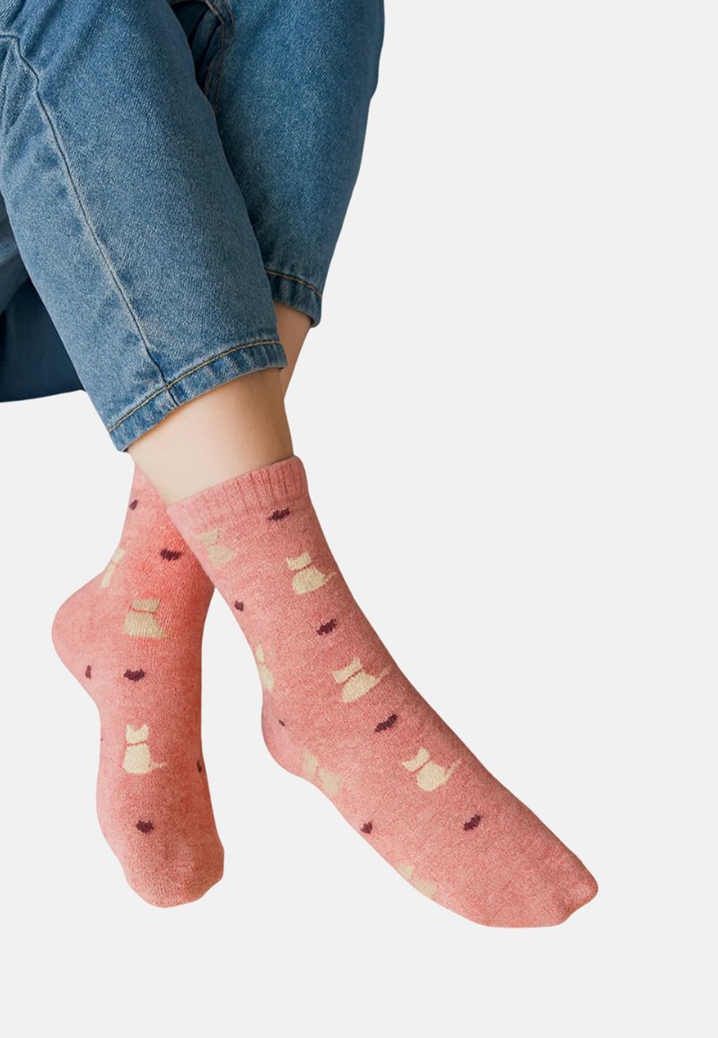 Rosa Baumwollsocken mit cremefarbenen und kastanienbraunen Mustern kleiner Schleifen. Knöchellang mit gerippten Bündchen, getragen zu blauen, verkürzten Jeans.