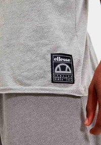 Camiseta de algodón gris con un parche de logo negro que presenta texto y diseño en blanco. La camiseta tiene mangas cortas y un corte relajado.