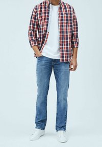 Rot- und marineblau kariertes Langarmhemd über einem weißen T-Shirt, kombiniert mit hellblauen Jeans und weißen Turnschuhen.