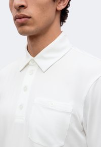 Homme portant un polo blanc boutonné avec col et poche poitrine à fermeture par bouton.