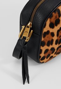Kosmetická taštička s leopardím vzorem v černé a hnědé barvě, s texturovanou kůží, zlatým zipem a černým koženým popruhem.