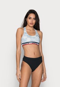 Ljusblå tie-dye sport-bh med svart midjebnad som har en röd och vit Levi's-logotyp; kombinerat med svarta högmidjade bikiniunderdelar.