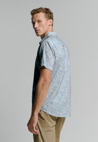 Korte mouwen overhemd met knoop in lichtblauw met een paisleypatroon. Gemaakt van zachte stof met een relaxte pasvorm en een kleine achtervent.