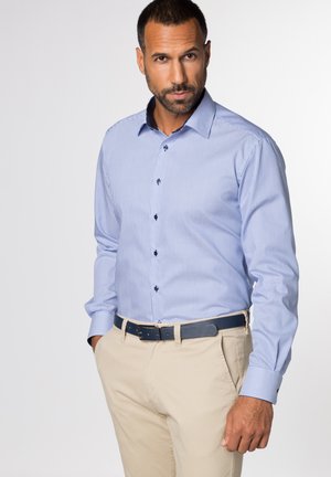 Gestreepte blauwe shirt met lange mouwen en button-down kraag, gecombineerd met beige broek en een blauwe riem, met donkere knopen en manchetten.