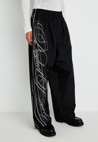 Black, loose-fitting pants with an elastic waistband, featuring white graphic designs and lines along the sides. Textured fabric and straight legs.
