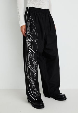 Black, loose-fitting pants with an elastic waistband, featuring white graphic designs and lines along the sides. Textured fabric and straight legs.