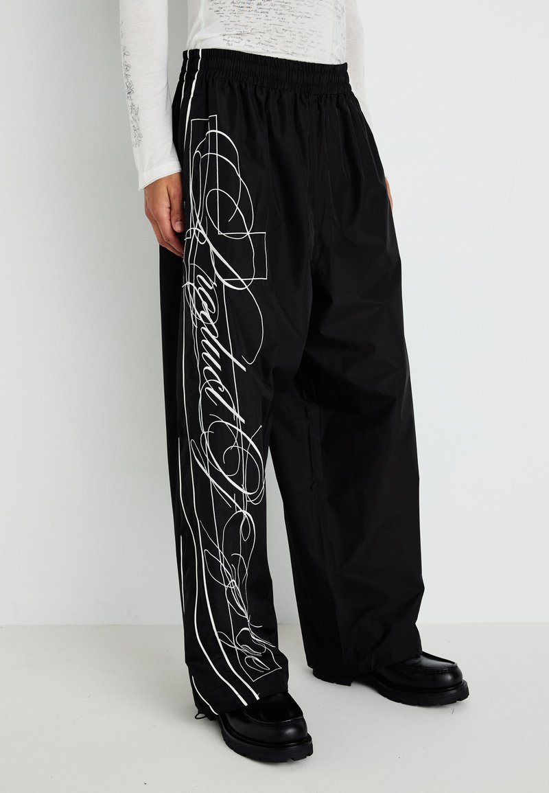 Black, loose-fitting pants with an elastic waistband, featuring white graphic designs and lines along the sides. Textured fabric and straight legs.