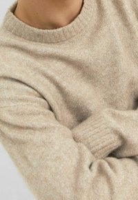 Pull beige en maille avec un col rond et des poignets côtelés, présentant une texture douce et un motif chiné subtil sur l'ensemble.