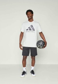Férfi világosszürke póló fekete és szürke mintázattal ellátott Adidas logóval és "BASKETBALL" felirattal, fekete rövidnadrággal és kosárlabdával párosítva.