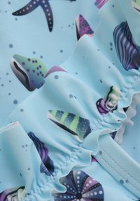 Ljusblått tyg med ett mönster av färgglada havsdjur, inklusive sjöstjärnor och snäckor, med vågiga kanter och fina sömmar.