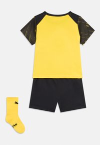 Ensemble de sport jaune et noir composé d'un t-shirt à manches courtes avec des manches à motifs, de shorts noirs et d'une paire de chaussettes jaunes.