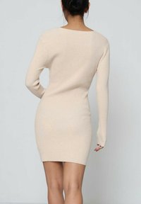 Robe moulante en tricot côtelé beige avec des manches longues et un décolleté profond dans le dos, conçue pour épouser étroitement la taille et les hanches.