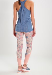 Top sin mangas azul con detalle de lazo en la parte posterior; leggings de estampado en rosa y azul con una mezcla de formas; zapatillas deportivas grises.