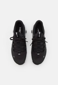 Scarpe sportive nere con tomaia in mesh strutturato, dettagli grigi e suole bianche a contrasto. Presentano lacci piatti e un design minimalista.