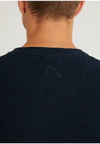 Granatowy sweter dzianinowy z teksturowanym wzorem, z okrągłym dekoltem i drobnym detalem w postaci stichego szwu z tyłu. Tkanina wydaje się miękka i lekka.