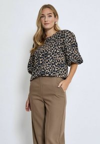 Bluzka w leopardzi wzór w kolorze brązowym i czarnym, z krótkimi bufkowymi rękawami i luźnym krojem, zestawiona z brązowymi spodniami o wysokim stanie.