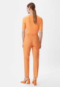 Pomarańczowa, prążkowana bluzka z krótkim rękawem w zestawieniu z dopasowanymi pomarańczowymi spodniami oraz pasującymi butami na obcasie w kształcie bloku. Widok z tyłu podkreśla elegancki design.