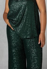 Grön paljettopp och matchande vida byxor, med en mjuk textur och lös passform, samt synliga sidofickor på byxorna.