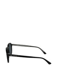 Occhiali da sole neri Calvin Klein con una montatura arrotondata, lenti grigie sfumate e aste nere eleganti. Dettagli includono un discreto logo del marchio sul lato.
